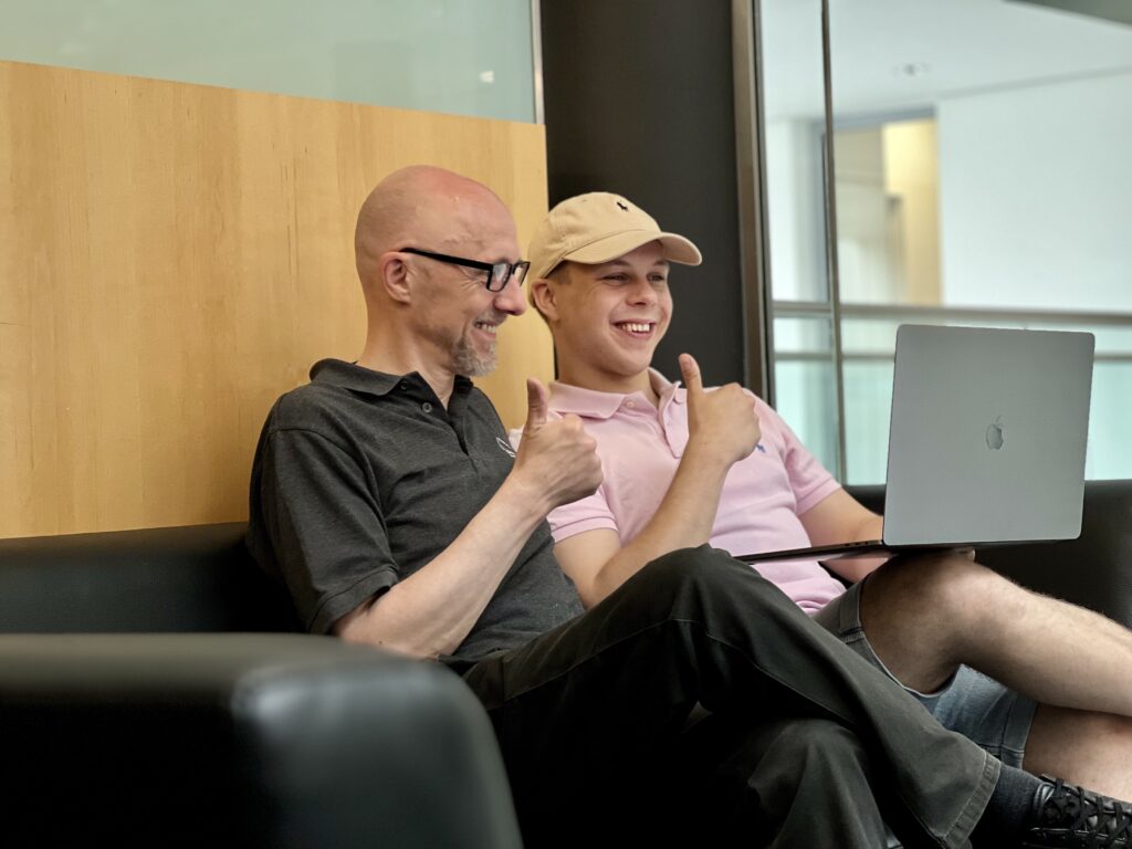 Das Bild zeigt Andreas und Dario gemeinsam im Büro sitzend vor einem Laptop.